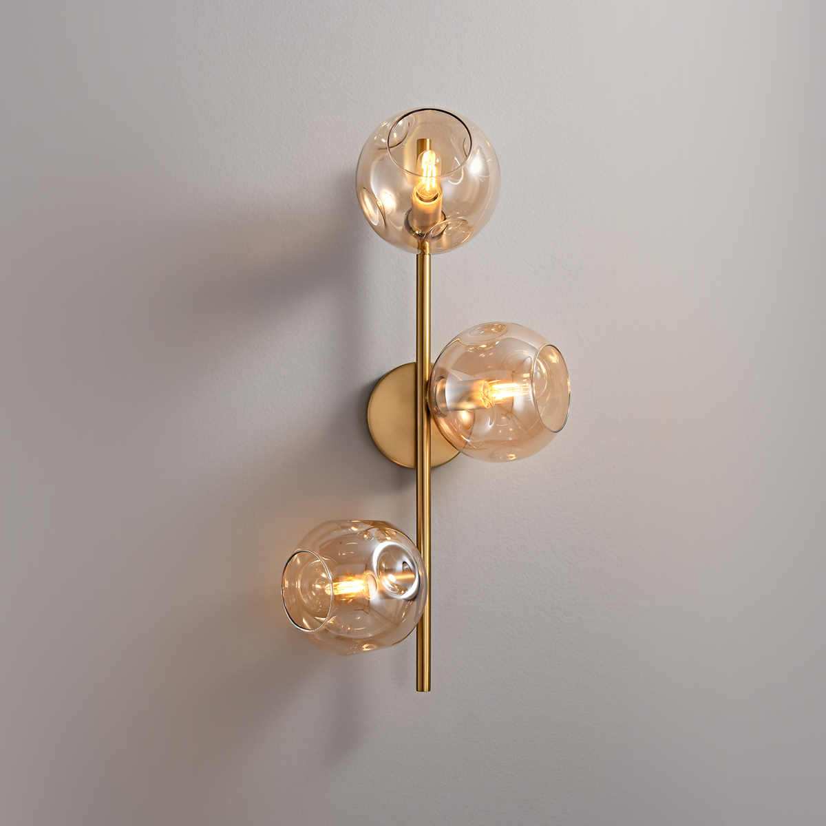 3-Light Modern Brass Wall Sconce 2 Angled view of modern gold wall lighting with illuminated amber glass.