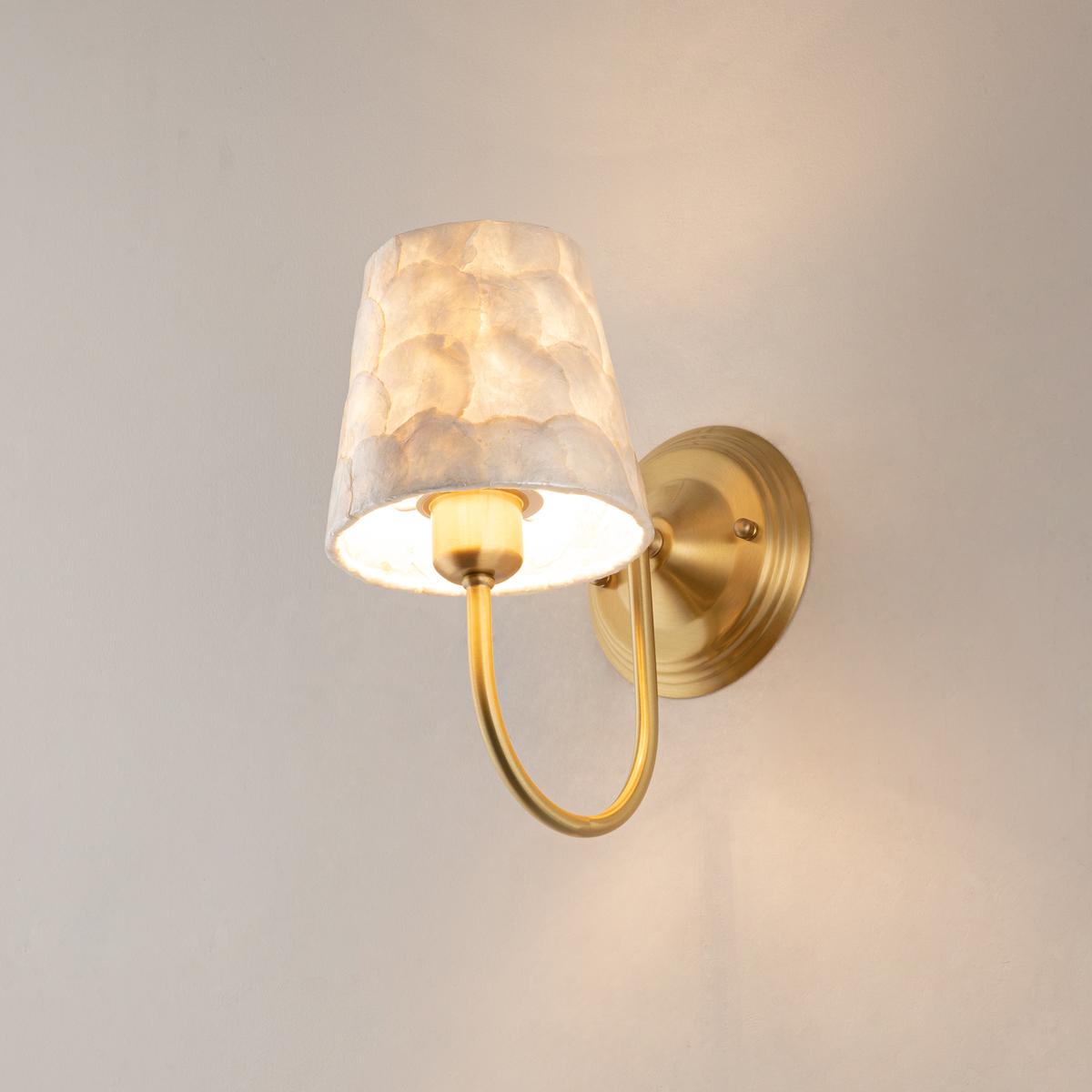 Modern Capiz Shell Wall Sconce 3 Underneath angled view of a coastal-style brass wall sconce with glowing shell lampshade showing the bulb socket.