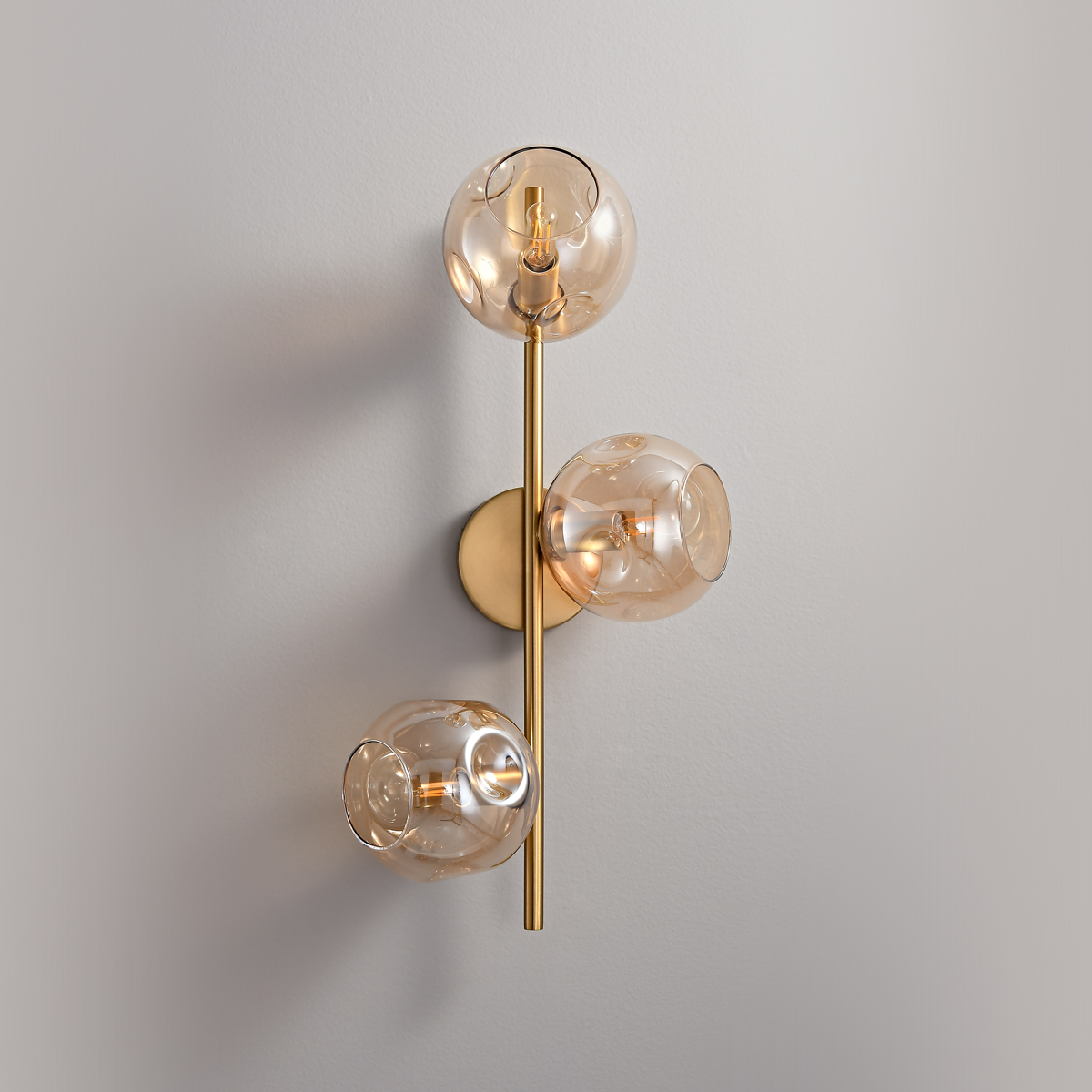 3-Light Modern Brass Wall Sconce 4 Close up of an illuminated mid-century modern amber glass globe sconce.