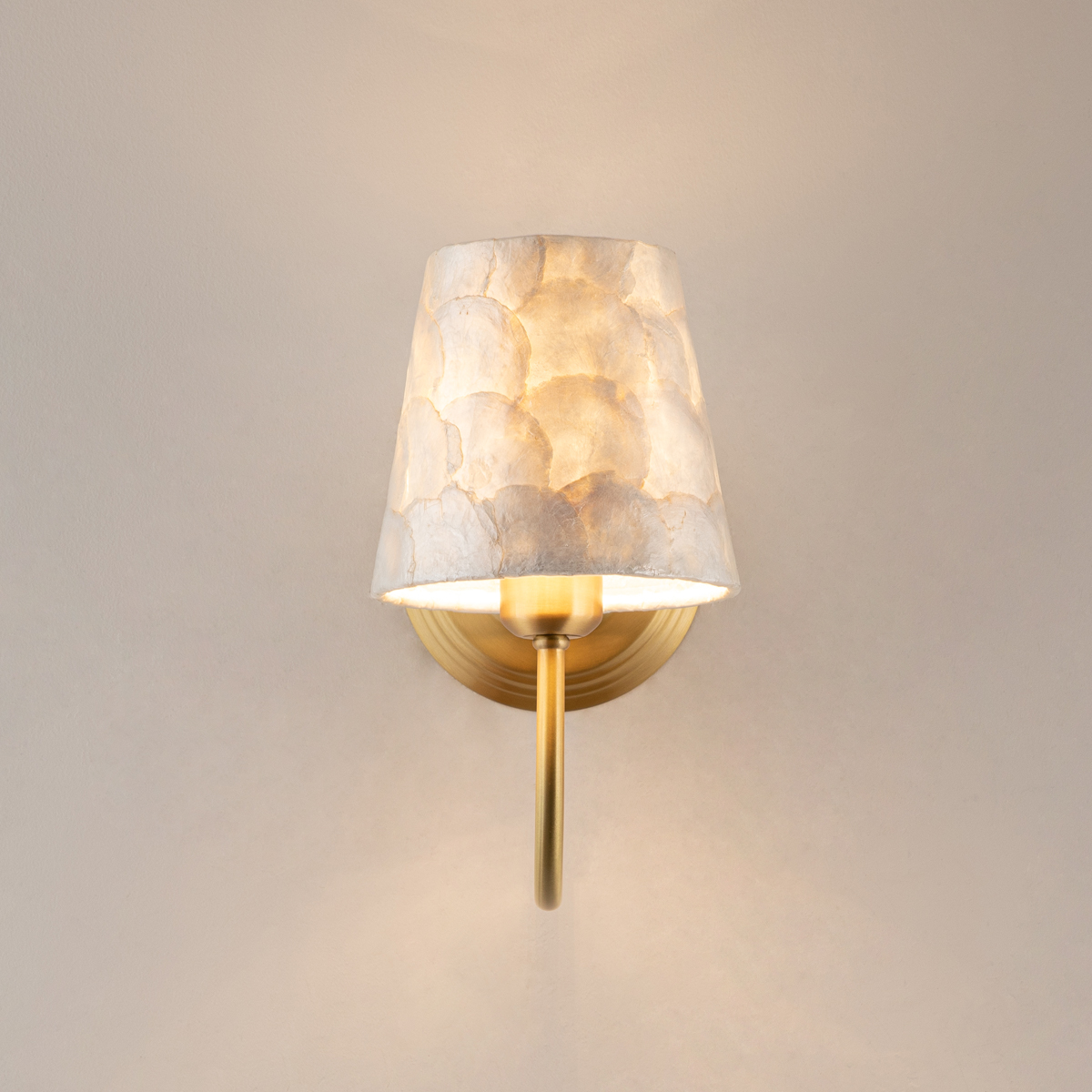 Modern Capiz Shell Wall Sconce 2 Front view of a gold brass wall light featuring a scalloped natural capiz shell shade glowing warmly.