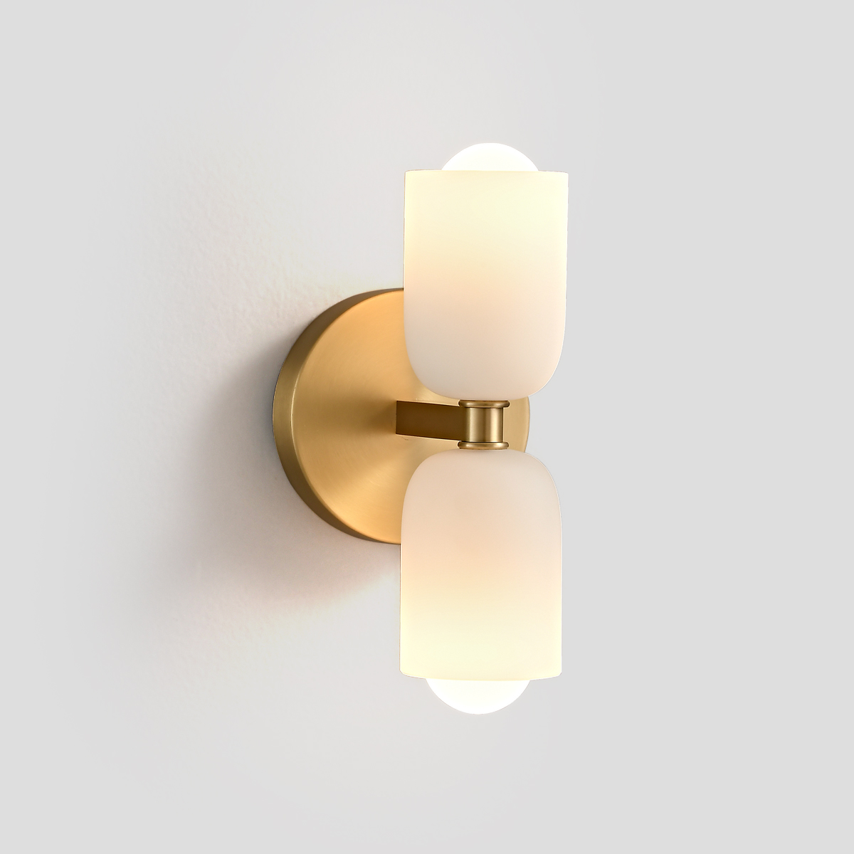 Mid-Century Modern Brass Wall Sconce 1 Front view of a modern brass wall sconce with dual frosted glass shades against a white wall.
