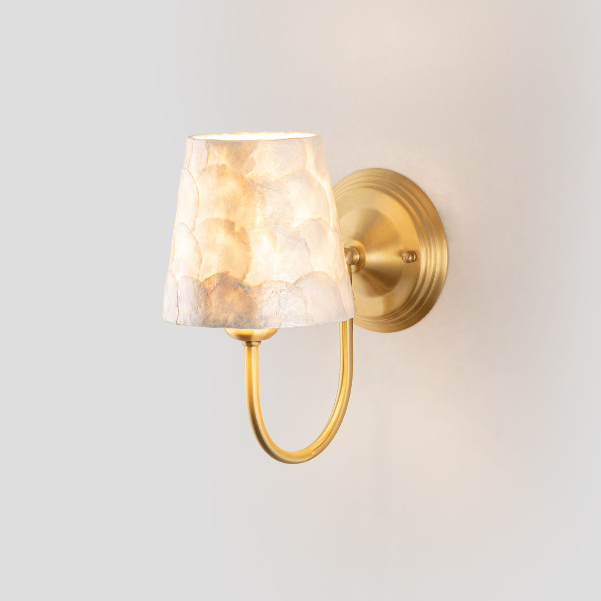 Modern Capiz Shell Wall Sconce 1 Single modern capiz shell wall sconce light fixture with brushed brass finish, illuminated on a clean background.